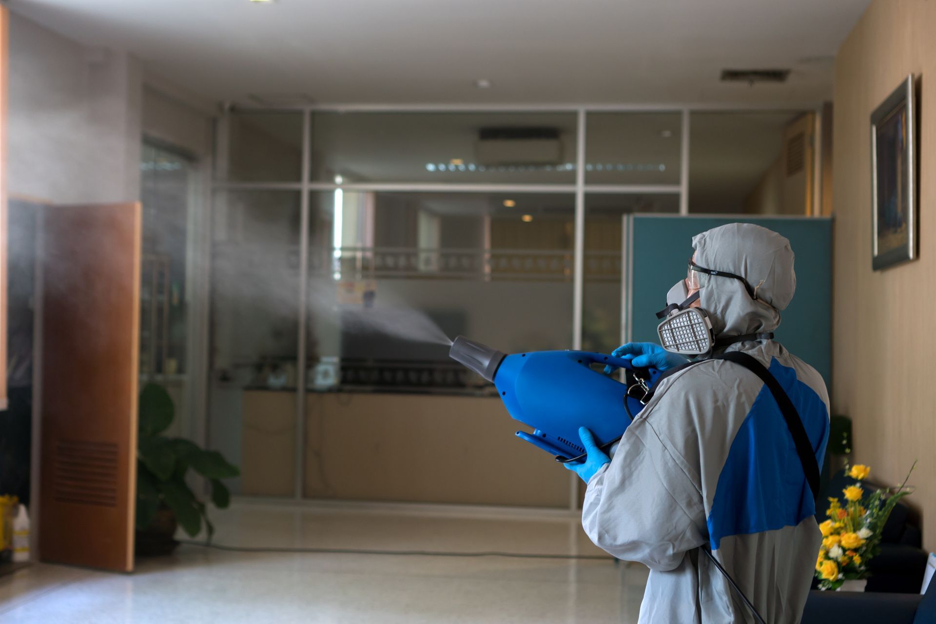 Person in protective suit spraying disinfectant in a building.