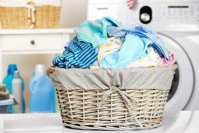 Overflowing laundry basket beside a washing machine in a bright laundry room