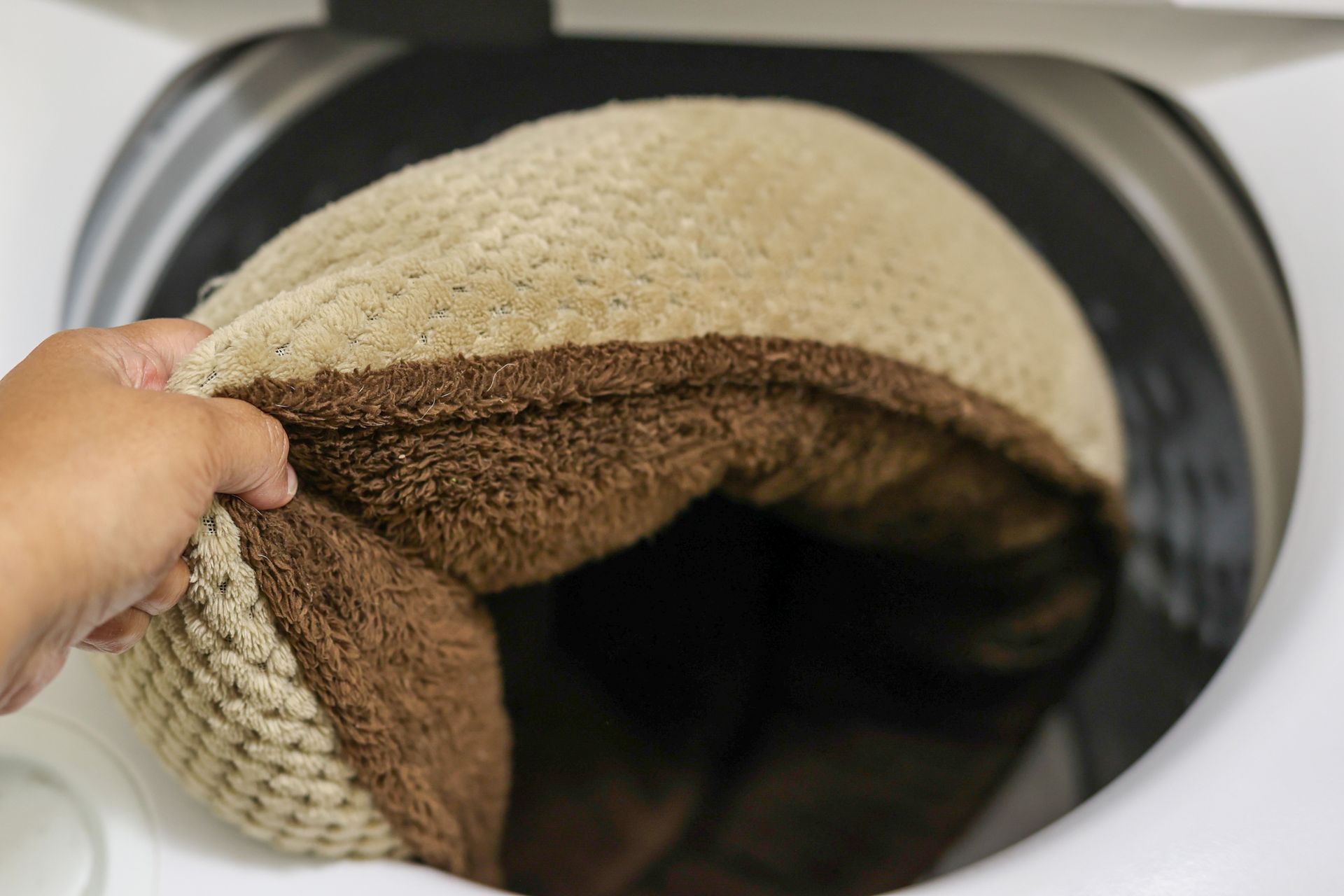 Hand placing a beige knit item into a washing machine drum