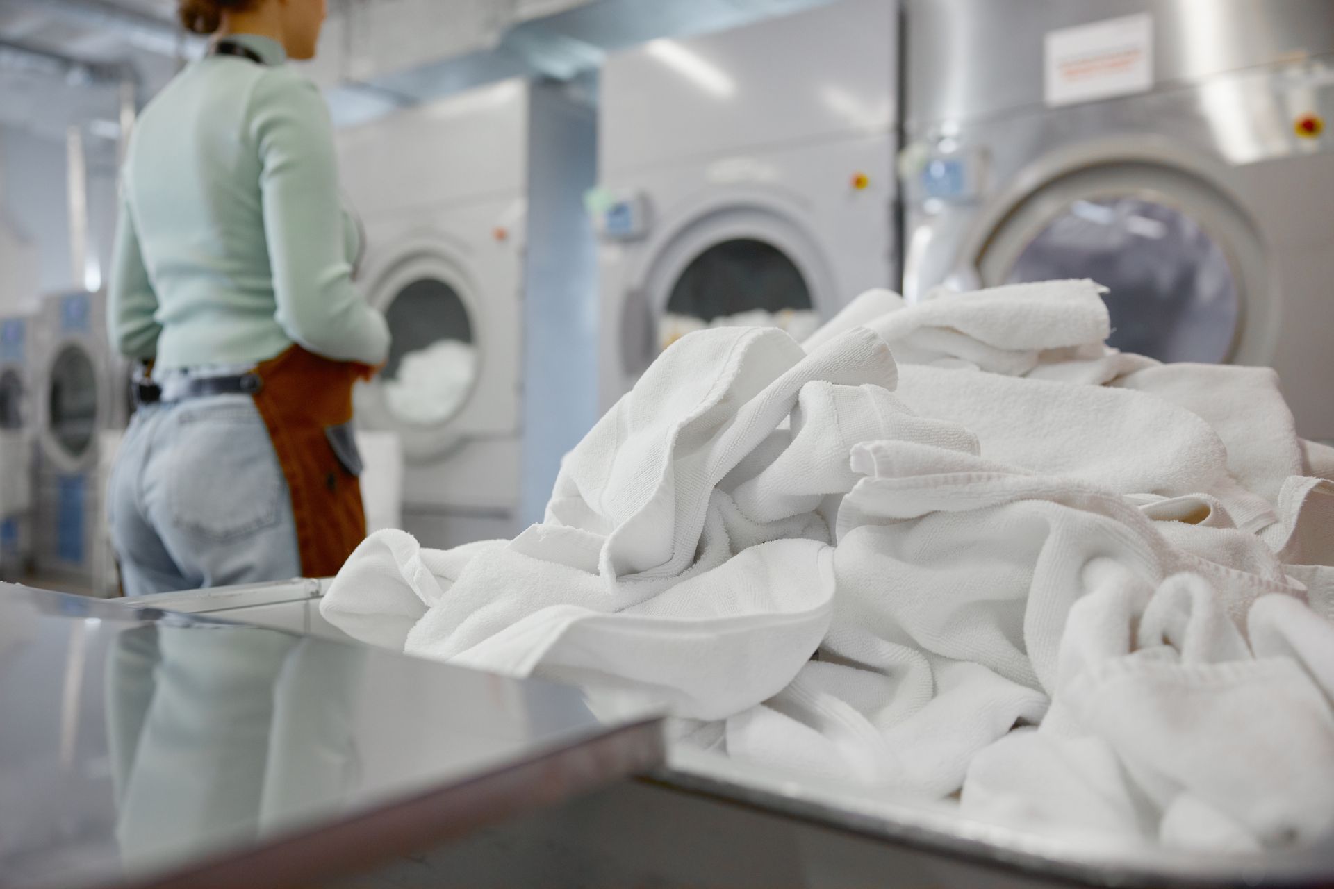 Laundry worker sorting white towels in a laundromat with industrial washers