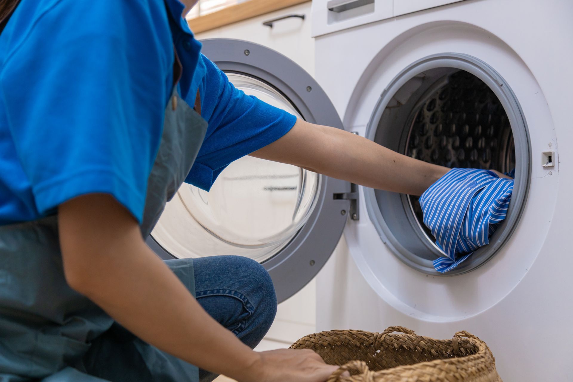 Person loading laundry into a front-loading washer beside a wicker basket