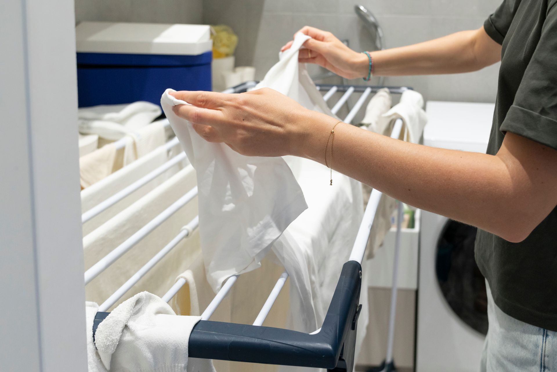 Hands hanging a white garment on a drying rack in a laundry room