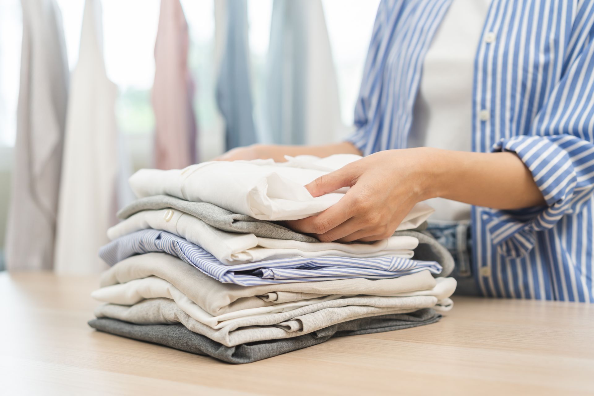 Person folding a stack of clothes on a table in a bright laundry room