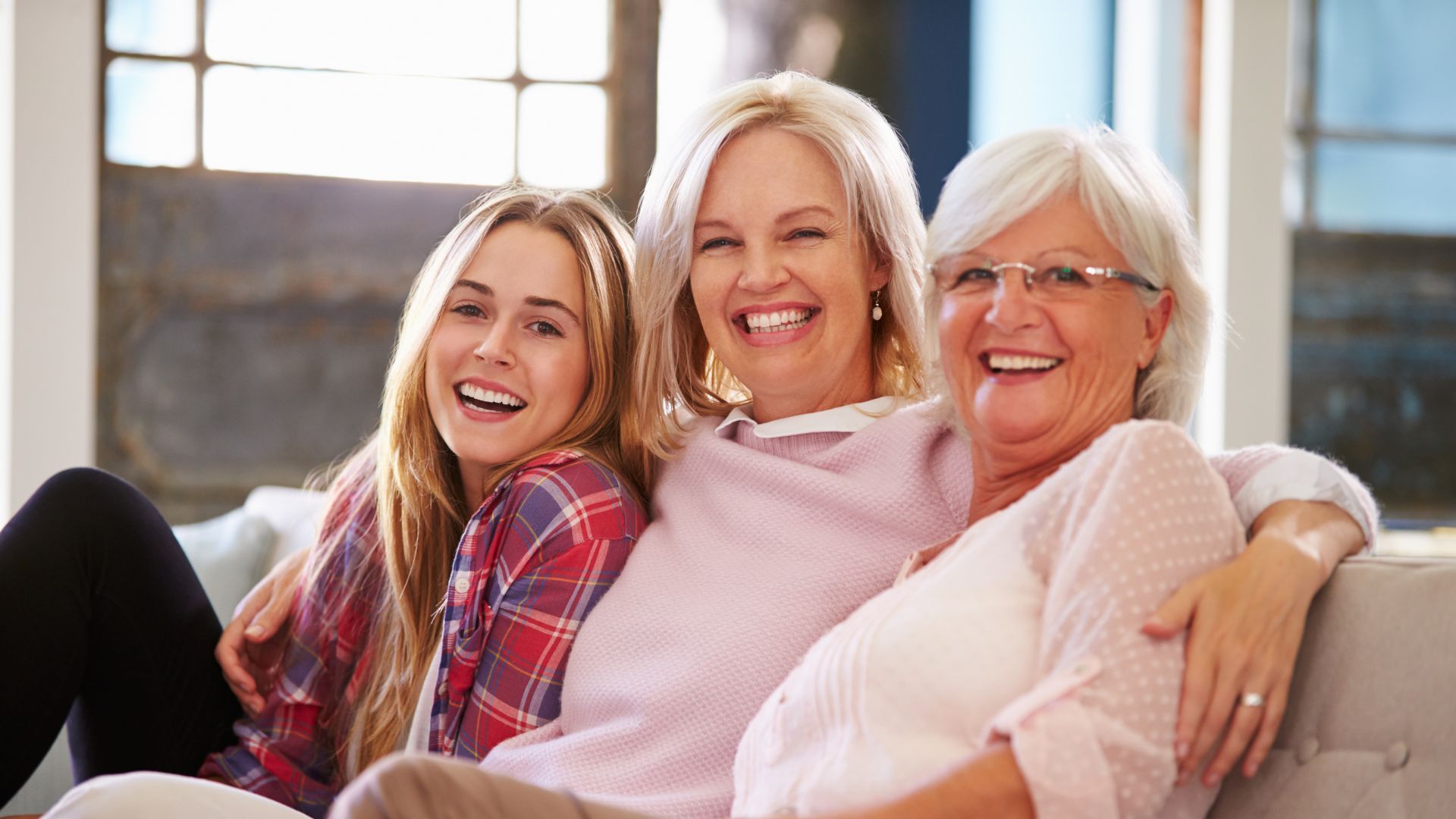 Three women are sitting on a couch and smiling for the camera.