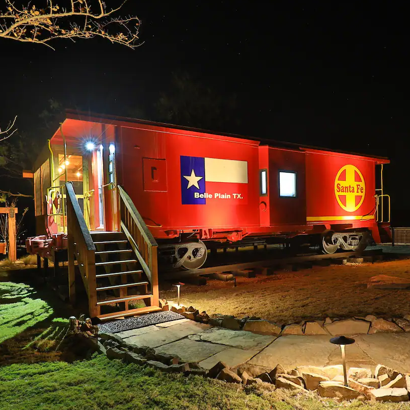 A red santa fe train car is lit up at night belle plain caboose airbnb in texas