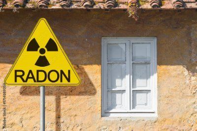 Yellow radon warning sign next to a white window on a beige wall.