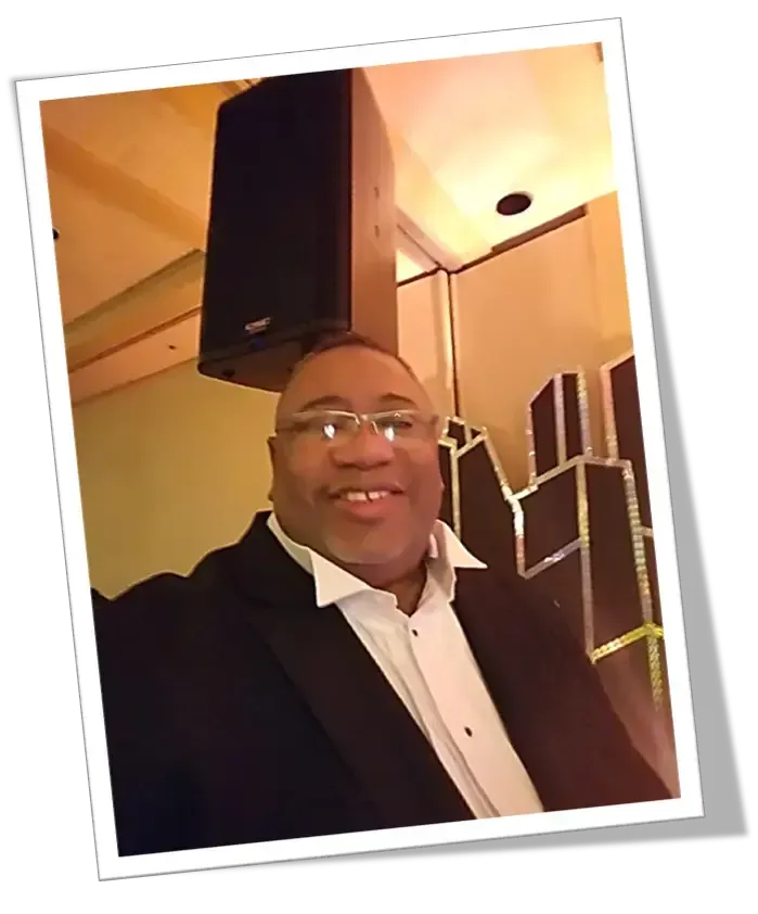 A man in a tuxedo is taking a selfie in front of a speaker