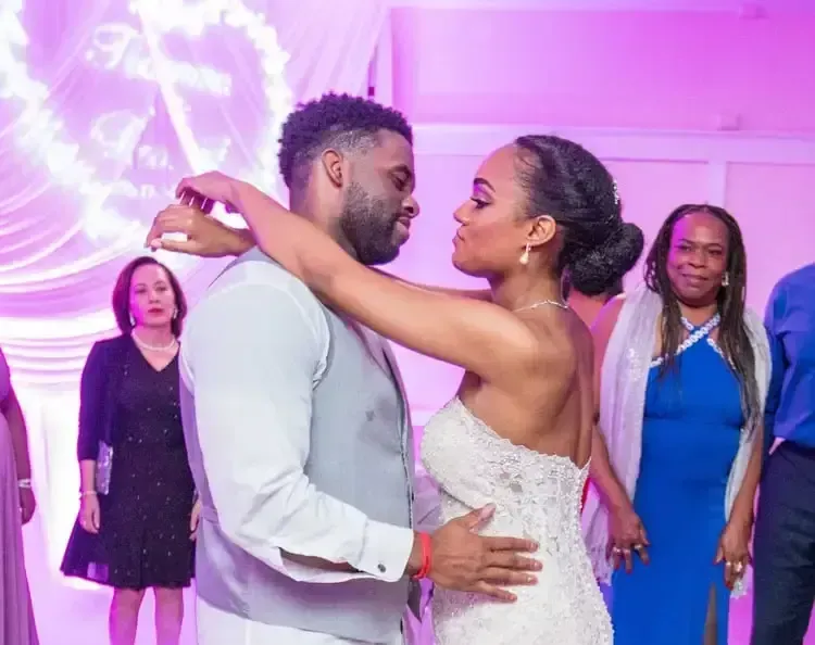 Couple dancing at a wedding, looking at each other, with other guests in the background.