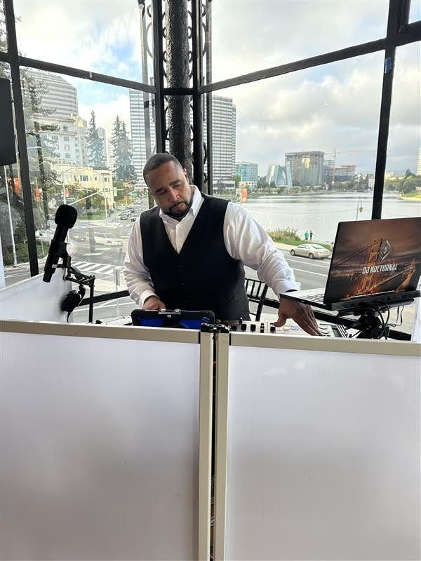 A man is playing music on a dj set in front of a large window.