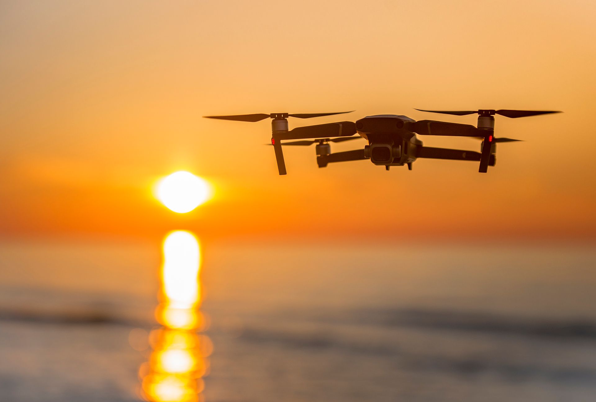 Drone che vola sull'oceano al tramonto; la sua silhouette si staglia contro un cielo e un'acqua di un arancione acceso.