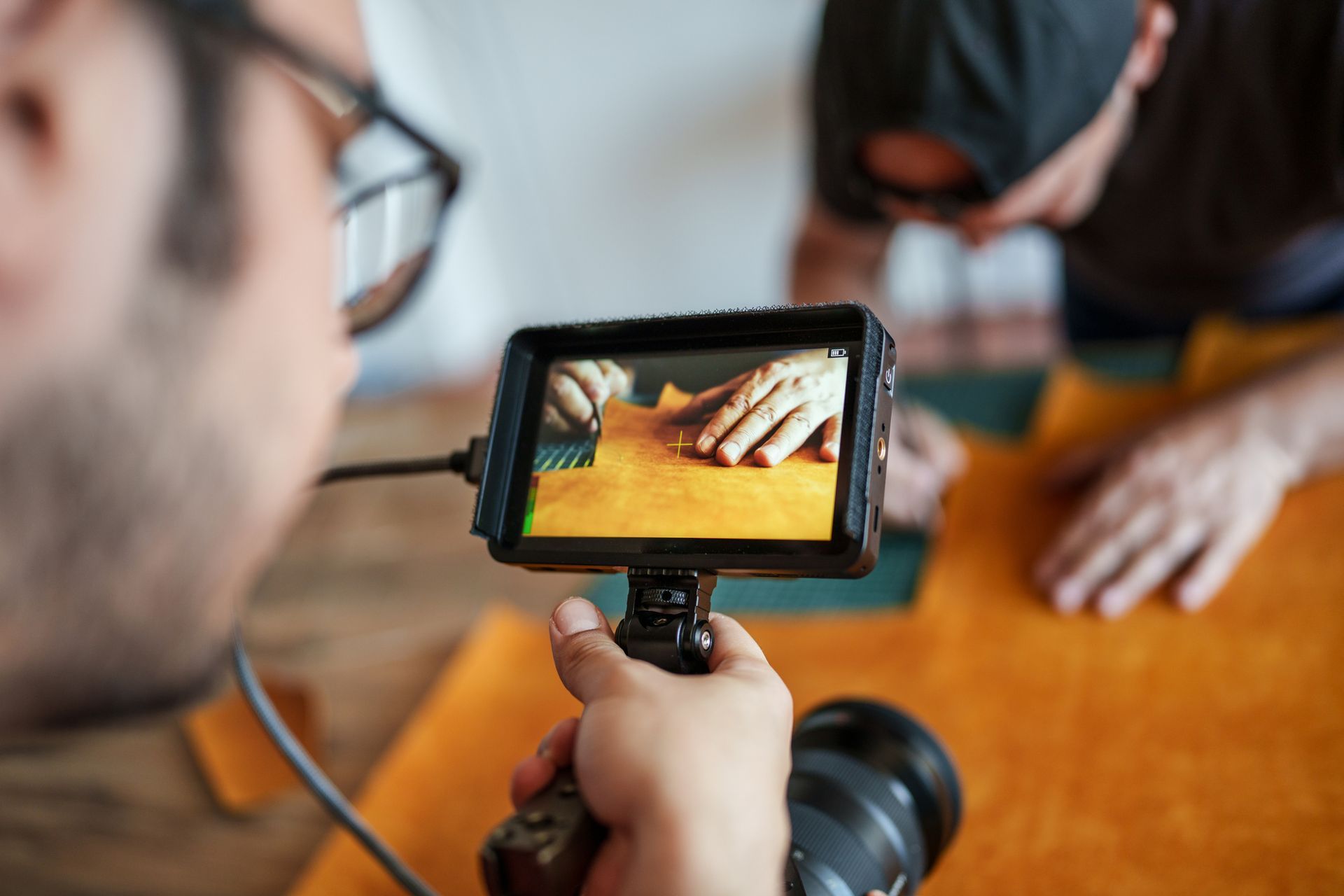 Uomo che filma le mani che lavorano la pelle, utilizzando un monitor per inquadrare l'inquadratura in un laboratorio.