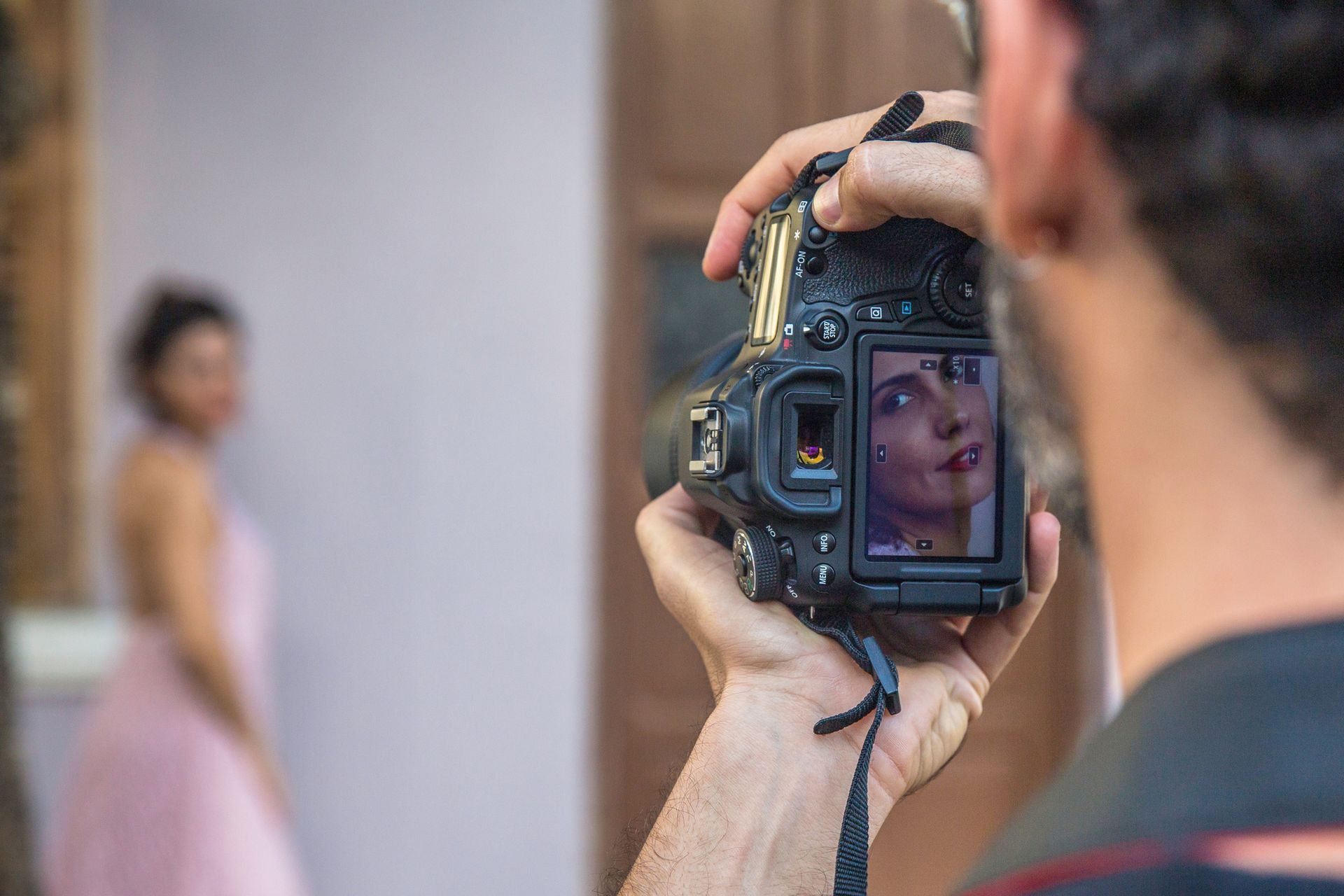 Fotografo con la macchina fotografica in mano, scatta una foto a una donna in abito rosa contro un muro.