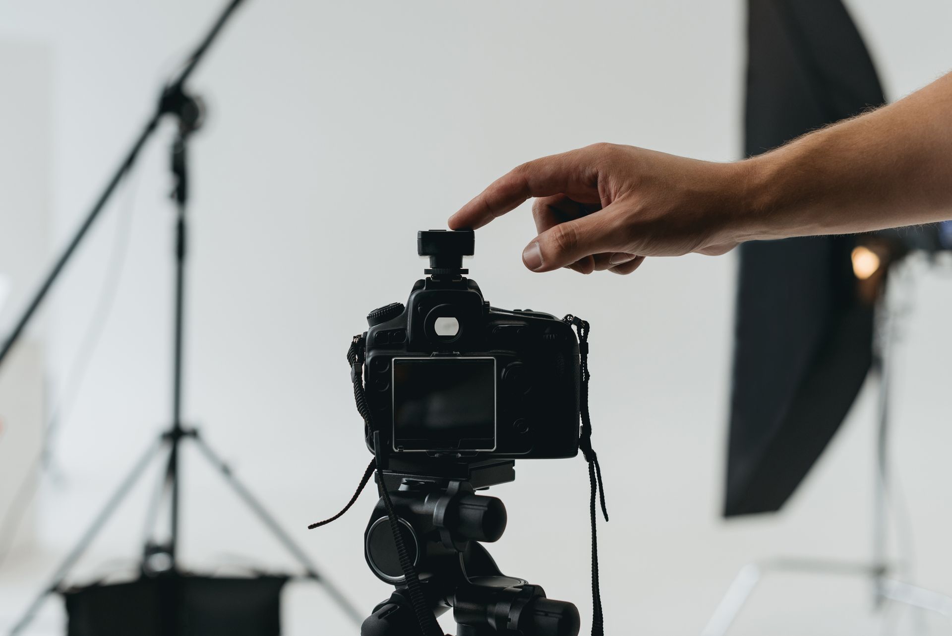 Una mano preme il flash su una macchina fotografica montata su un treppiede in uno studio fotografico.