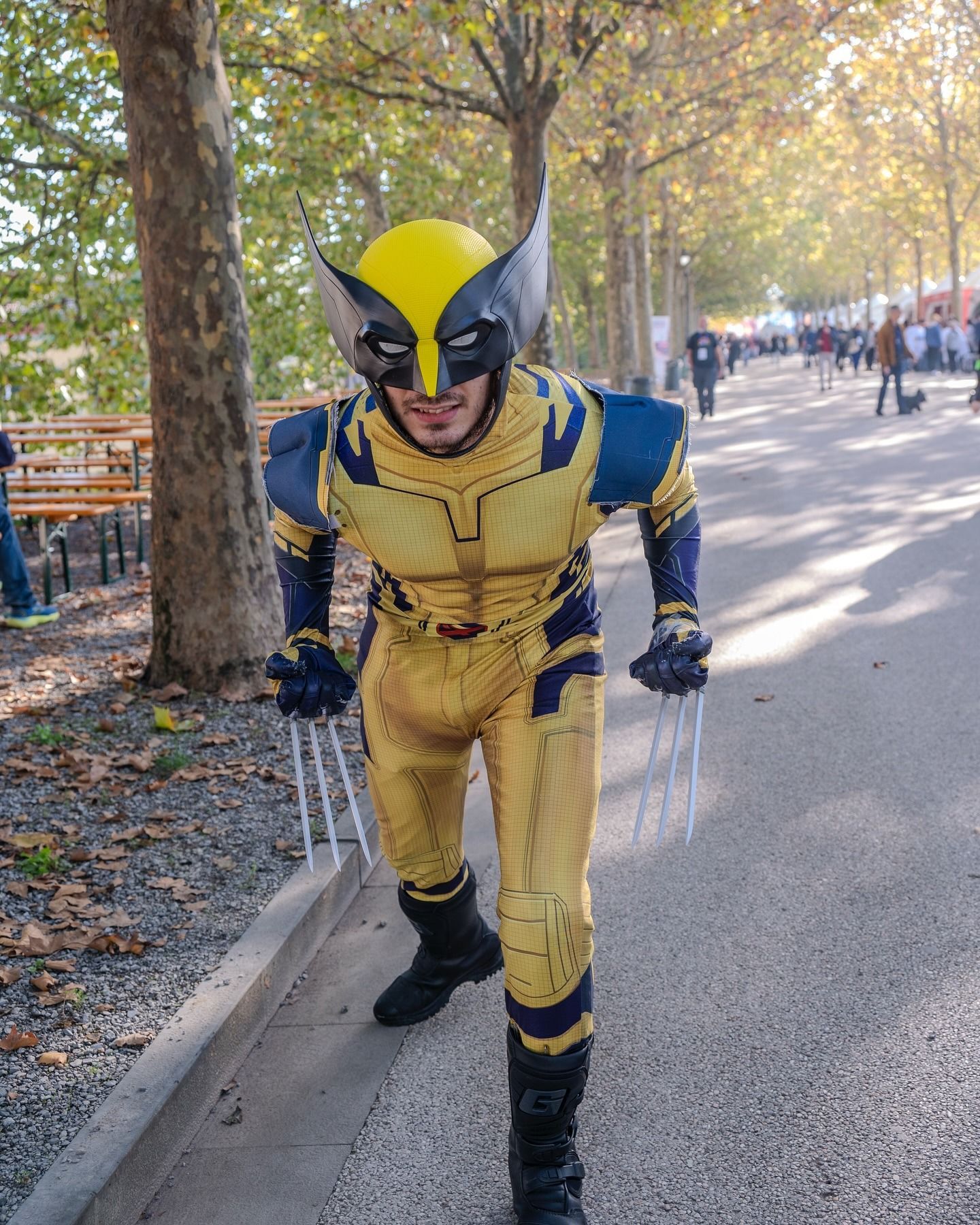 Un uomo in costume da Wolverine con artigli cammina su un sentiero. Indossa una tuta gialla e blu.
