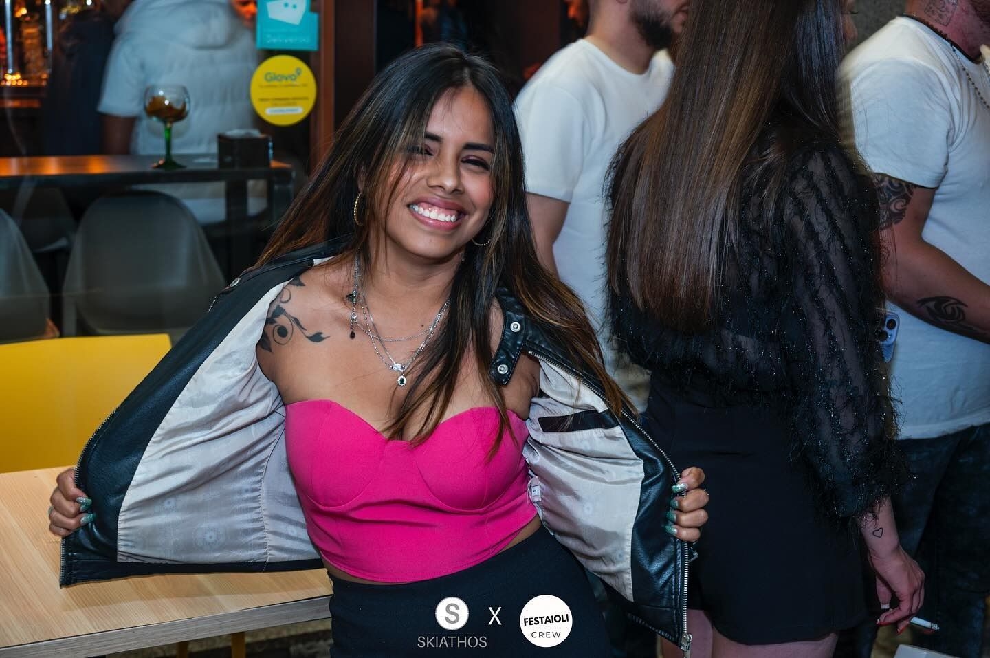 Una donna con un top rosa e una giacca nera sorride, durante una festa.