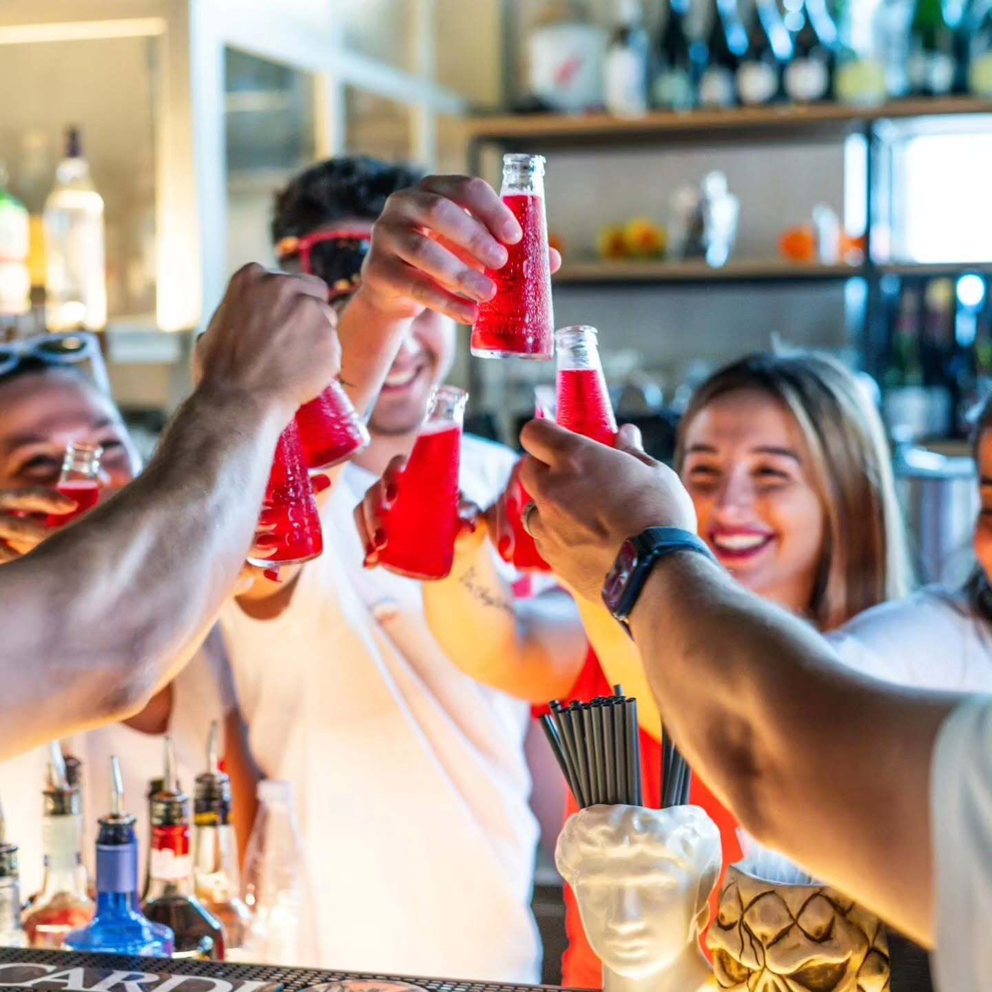 Un gruppo di amici brinda con cocktail rossi al bar, sorridendo e festeggiando.