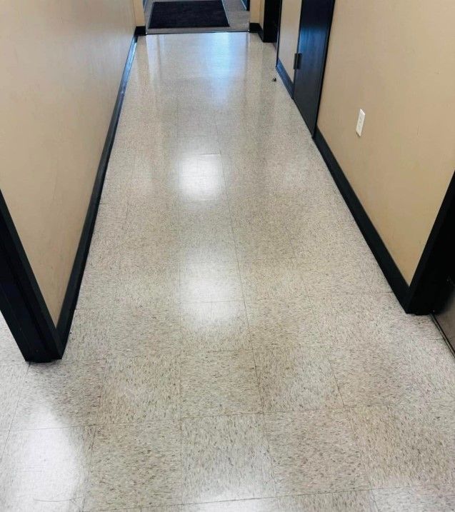 Hallway with light-colored speckled flooring, tan walls, and dark trim.