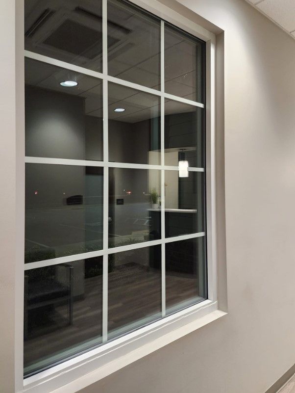 Window with white grid, reflecting an interior office space with grey walls and wood flooring.