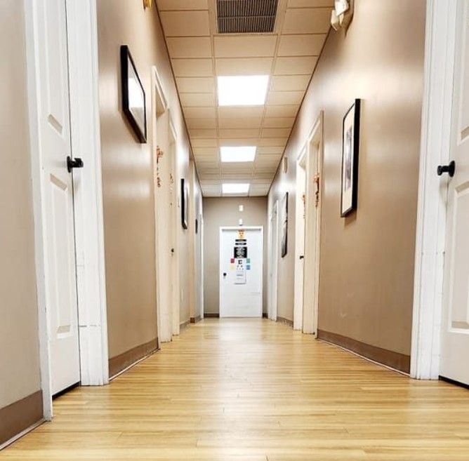 Long hallway with wooden floor, tan walls, white doors and ceiling lights.