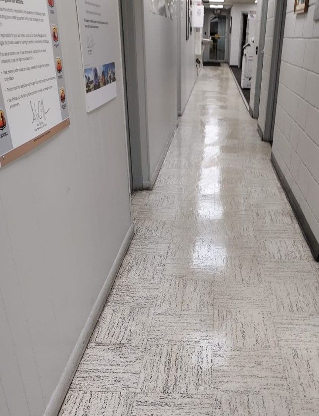 Long hallway with white walls and textured flooring, doors on both sides.