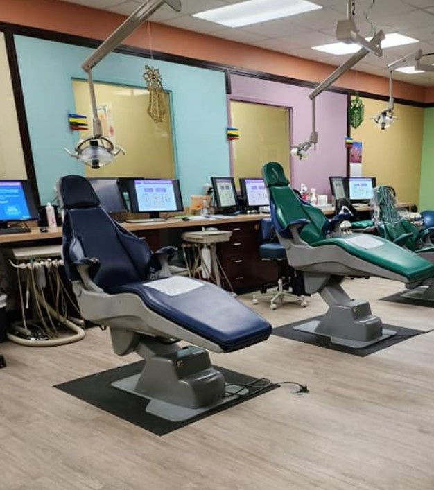 Dental clinic with three blue and green chairs, computers, and overhead lights.