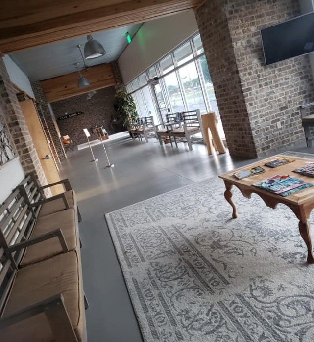 Spacious waiting area with benches, brick walls, large windows, rug, coffee table, and natural light.