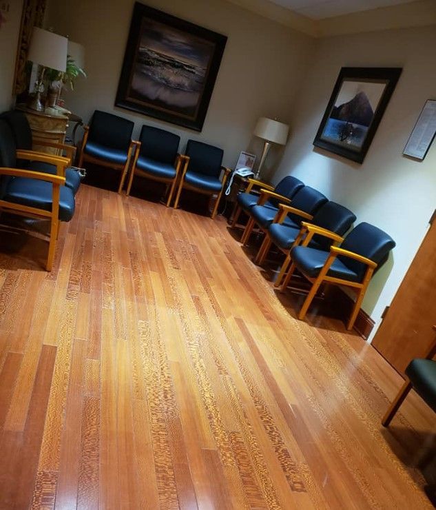 Waiting room with rows of blue chairs, wood floors, and framed artwork.