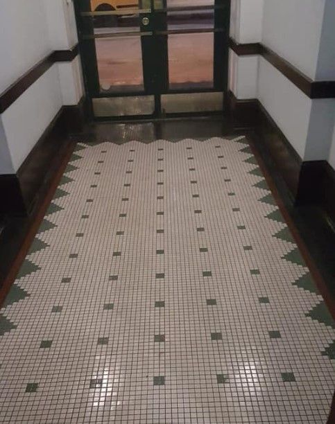Tiled entryway with zigzag border and dark green door. White and green square tiles.