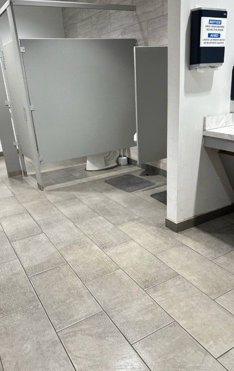 Public restroom with gray stalls, light-colored tiled floor, soap dispenser, and counter.