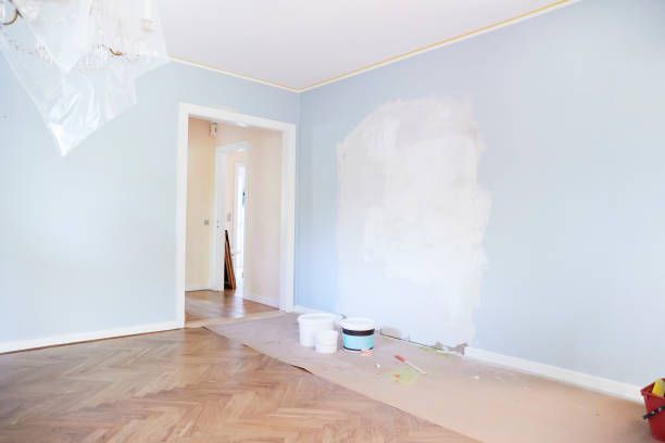 An empty room with blue walls and a wooden floor is being painted.