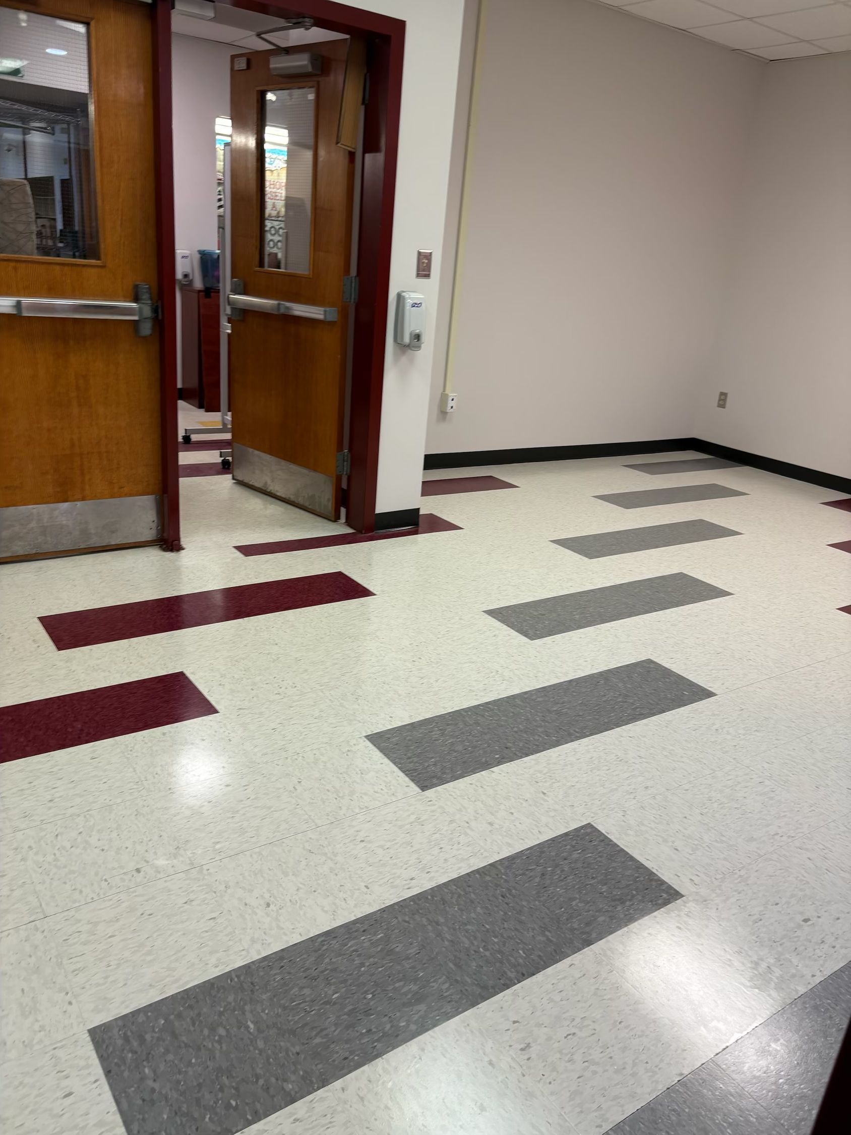 Hallway with white speckled floor, gray and maroon rectangles, and two brown doors.