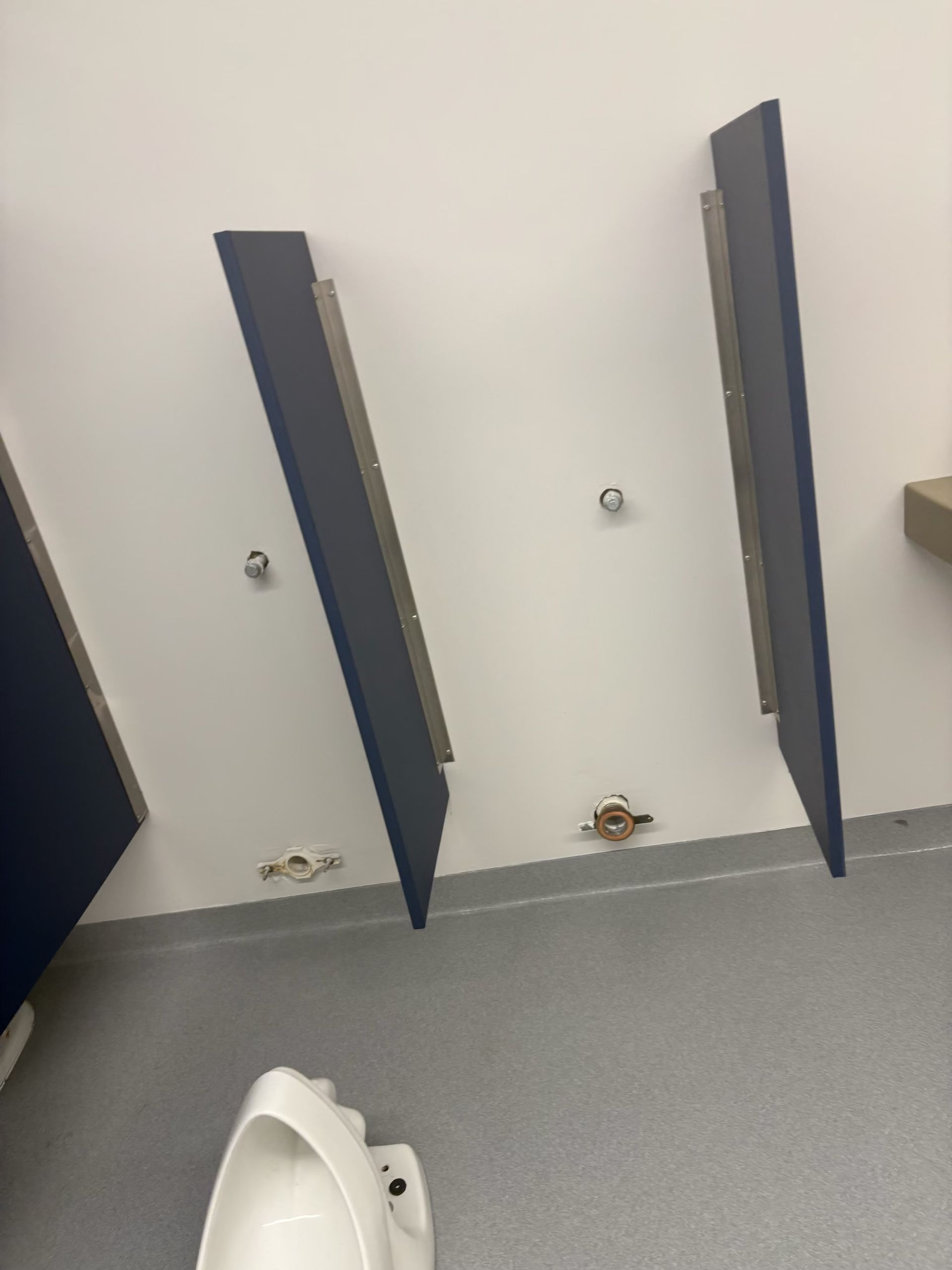 Public restroom with two blue-panel urinals and a urinal bowl in front of the wall.