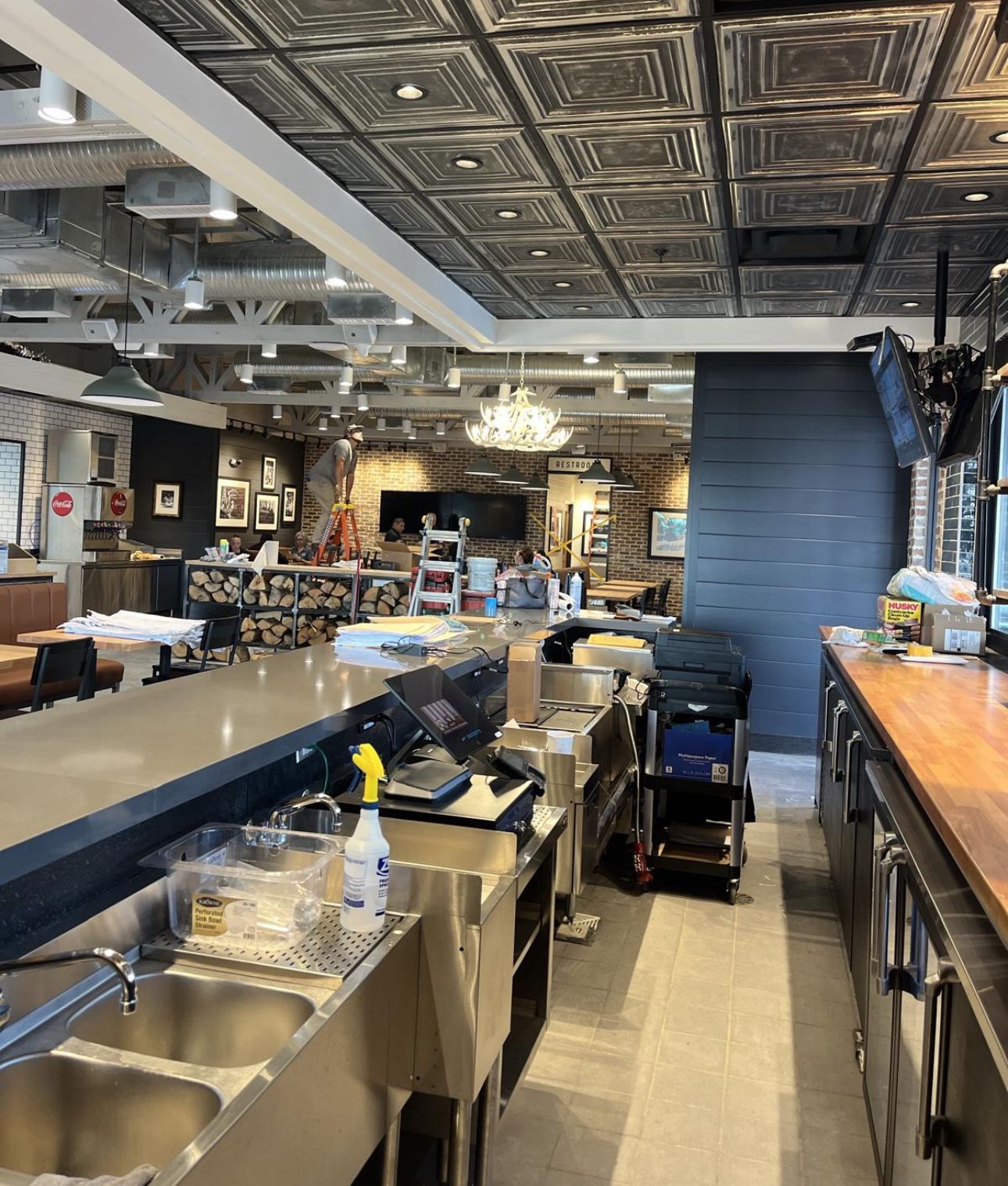 Interior of a commercial space, bar area with stainless steel sinks, equipment, and decorative ceiling tiles.