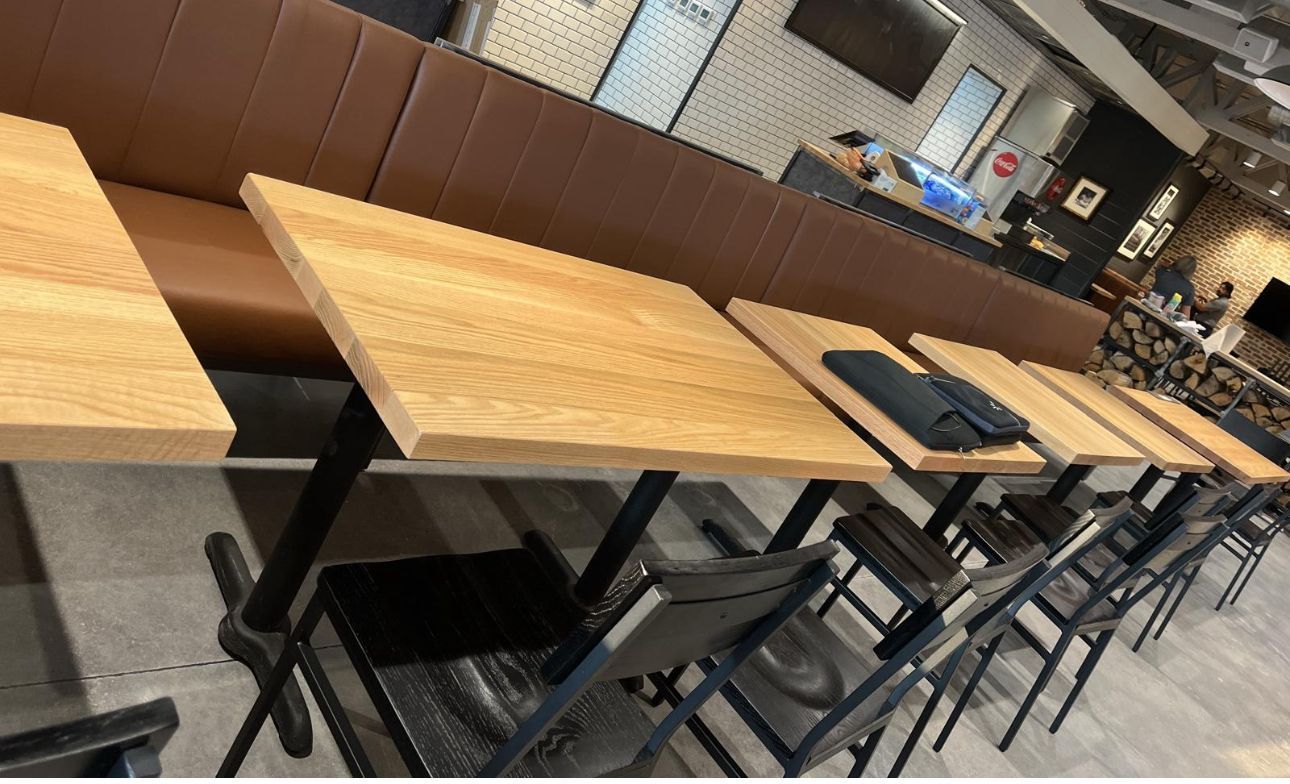 Restaurant seating: wooden tables with black chairs and a brown leather bench.