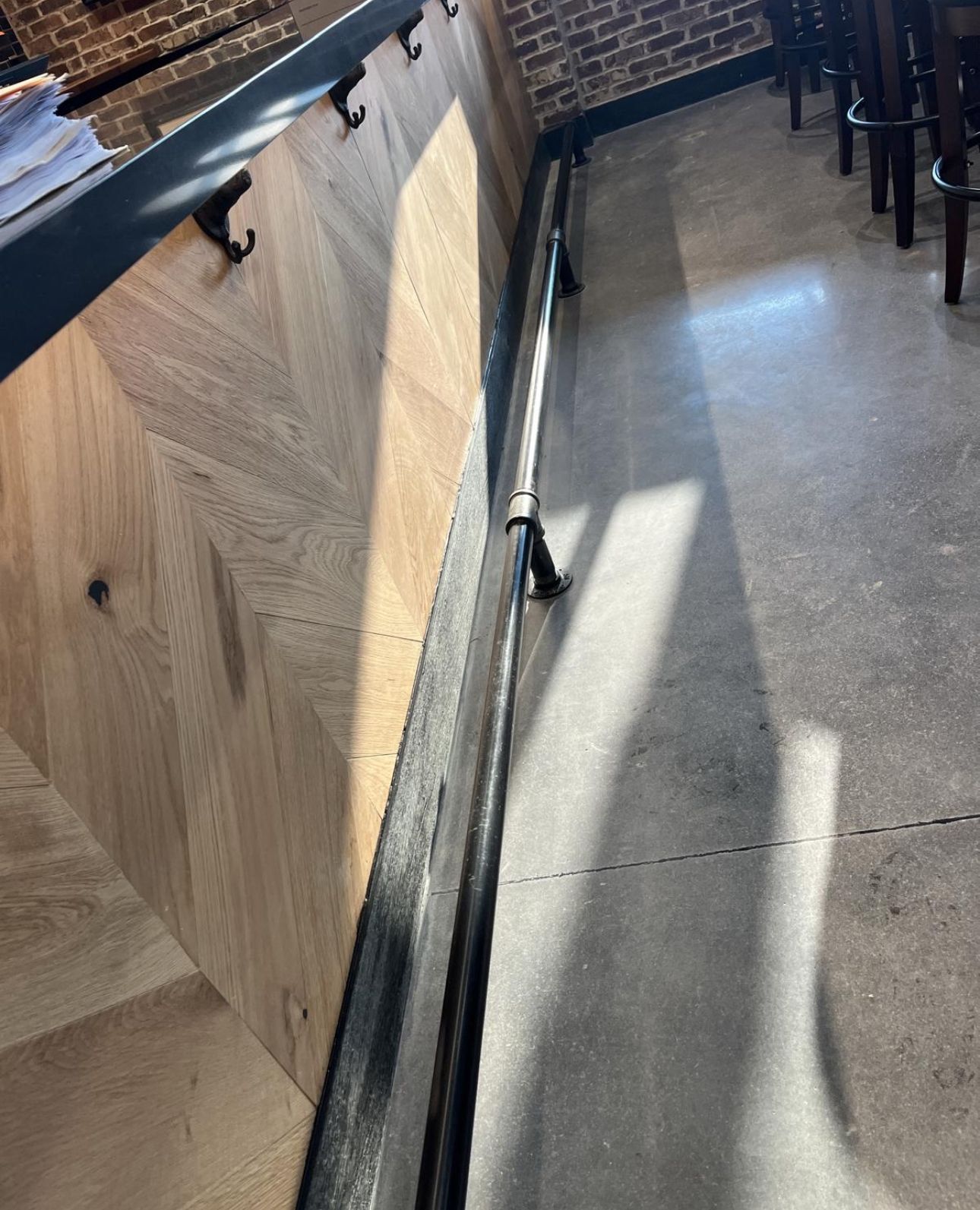 Wooden bar with dark metal accents and hooks, concrete floor, sunlight casting shadows.