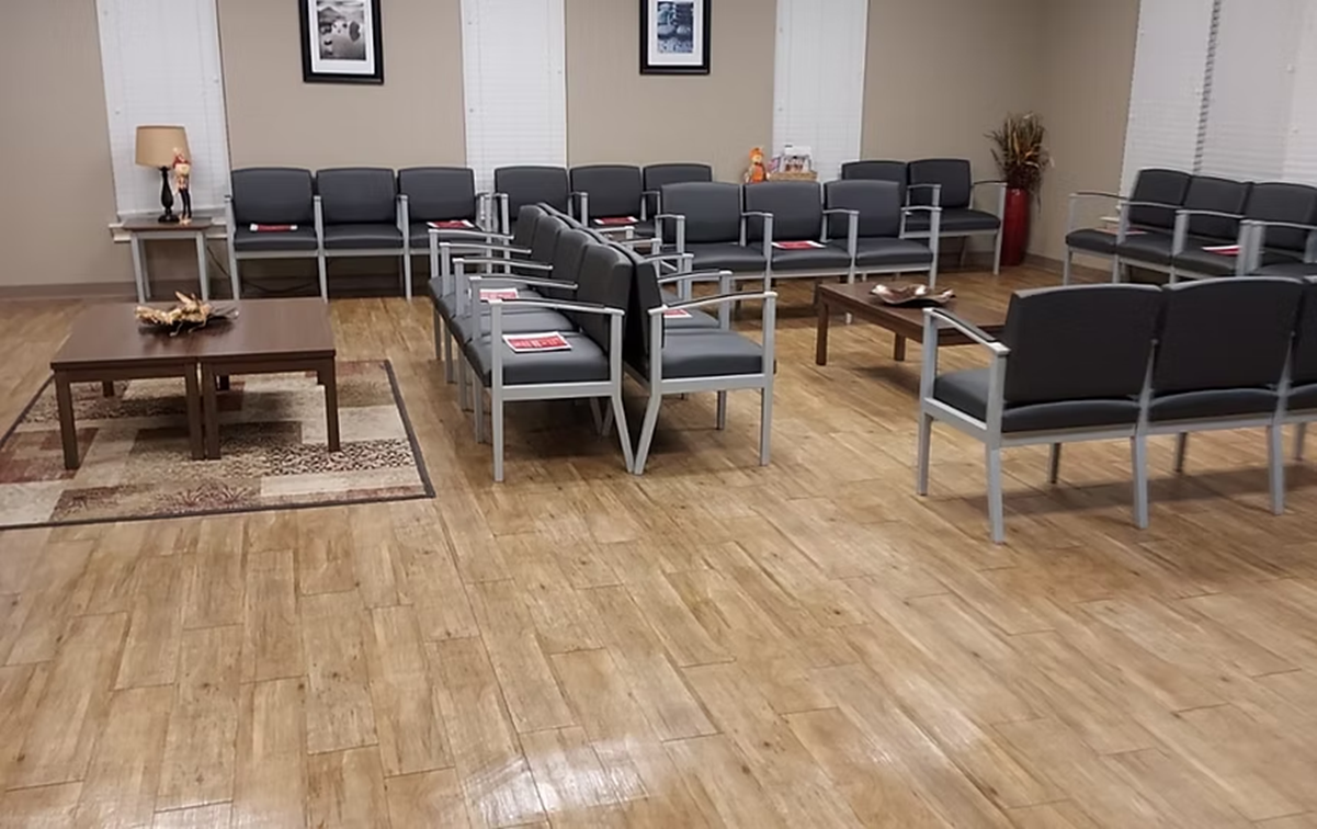 A waiting room with wooden floors and lots of chairs and tables.