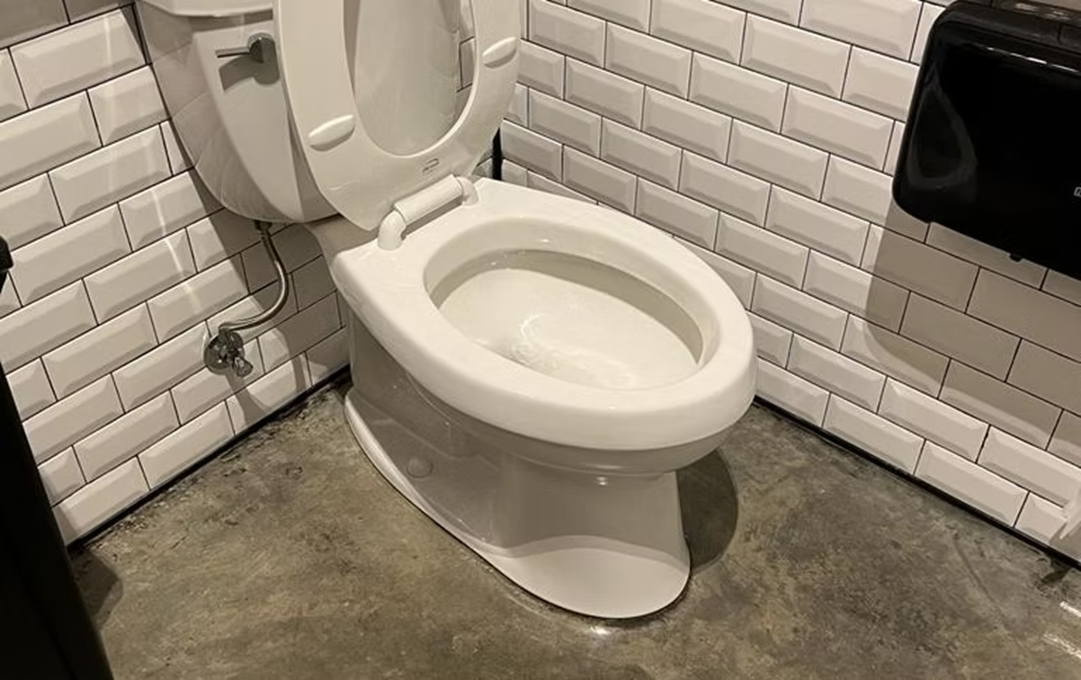 A white toilet is sitting in a bathroom next to a brick wall.