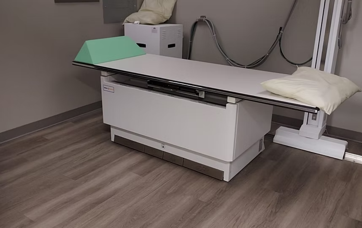 An x-ray machine is sitting on a wooden floor in a room.