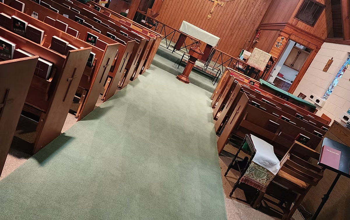 A church with rows of wooden pews and a green carpet