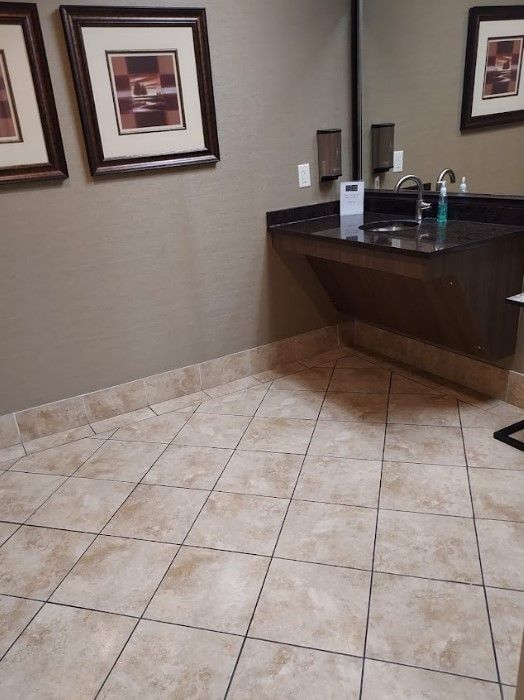 Public restroom with a dark sink, mirror, framed art, and tiled floor.