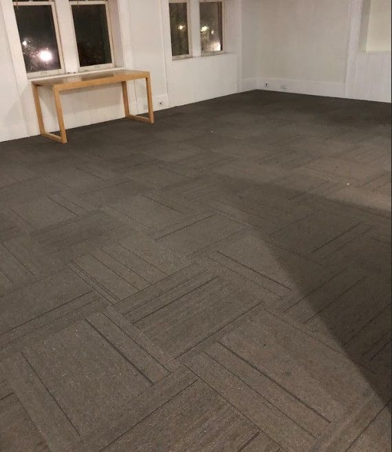 Empty room with gray patterned carpet, a wooden desk, and windows.