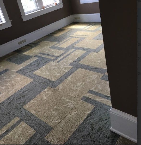 Room with geometric carpet in shades of beige, gray, and green, with brown walls and white trim.