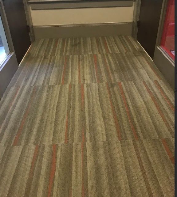Corridor with vertical striped carpet; brown, gray and orange tones. Doors on either side.