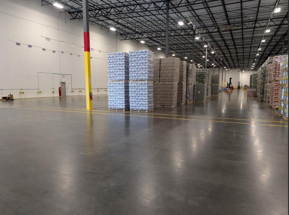 Warehouse interior, stacks of goods, concrete floor, high ceilings, several columns.