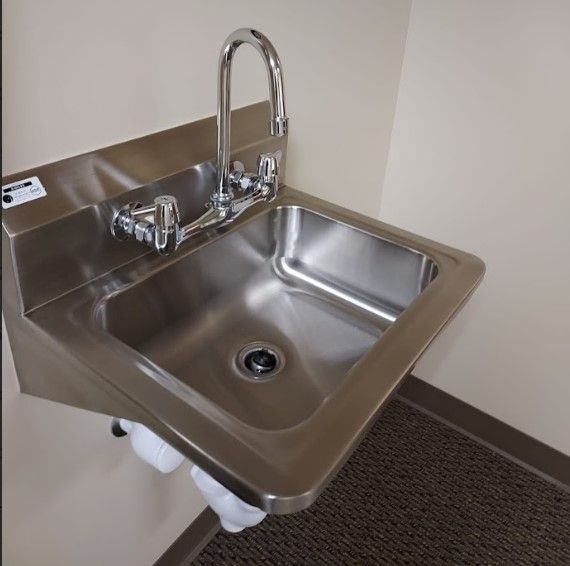 Stainless steel wall-mounted sink with a high-arc faucet in a corner of a room with off-white walls.