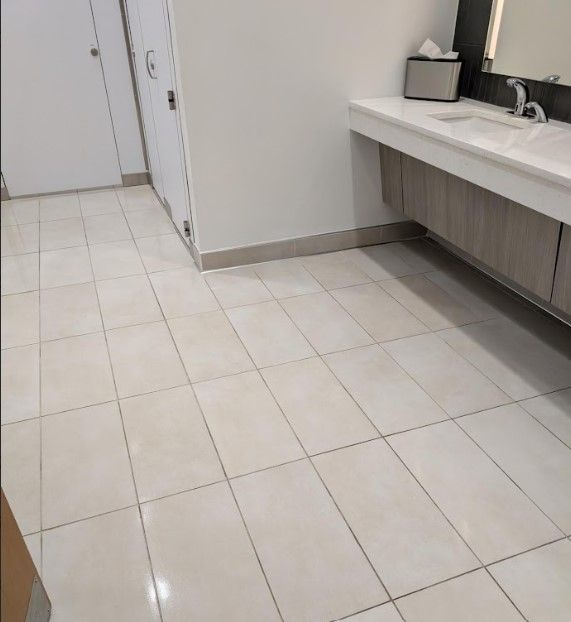 A public restroom with white tile floor, sinks, and two white stall doors.