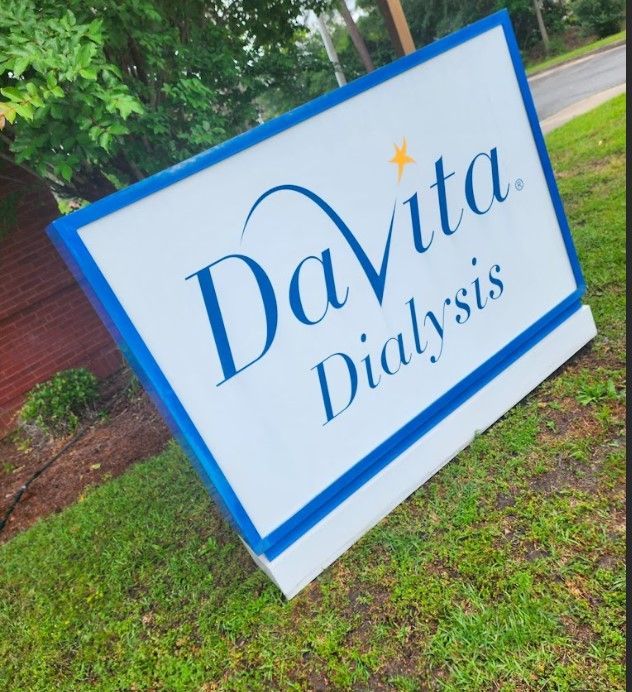DaVita Dialysis sign; white background, blue border and lettering; outdoor setting, grassy lawn.