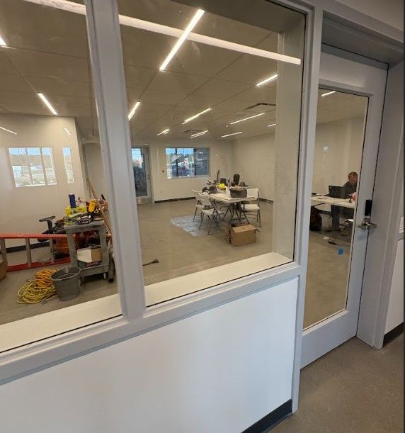 Interior of an office with tools, tables, and a person working, seen through glass doors.