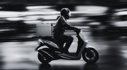 A man is riding a scooter with a box on the back.