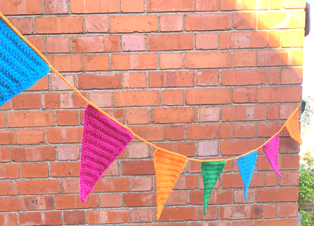Colorful triangular bunting hanging outside in front of a brick building.